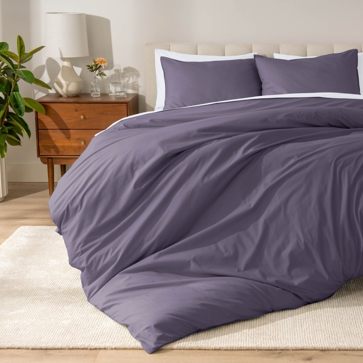 Percale bedding set on a bed in a bedroom with a wooden nightstand and lamp.