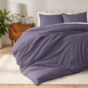 Percale bedding set on a bed in a bedroom with a wooden nightstand and lamp.