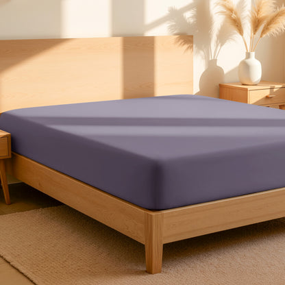 Fitted sheet on a bed in a bedroom setting with a lamp and plant.