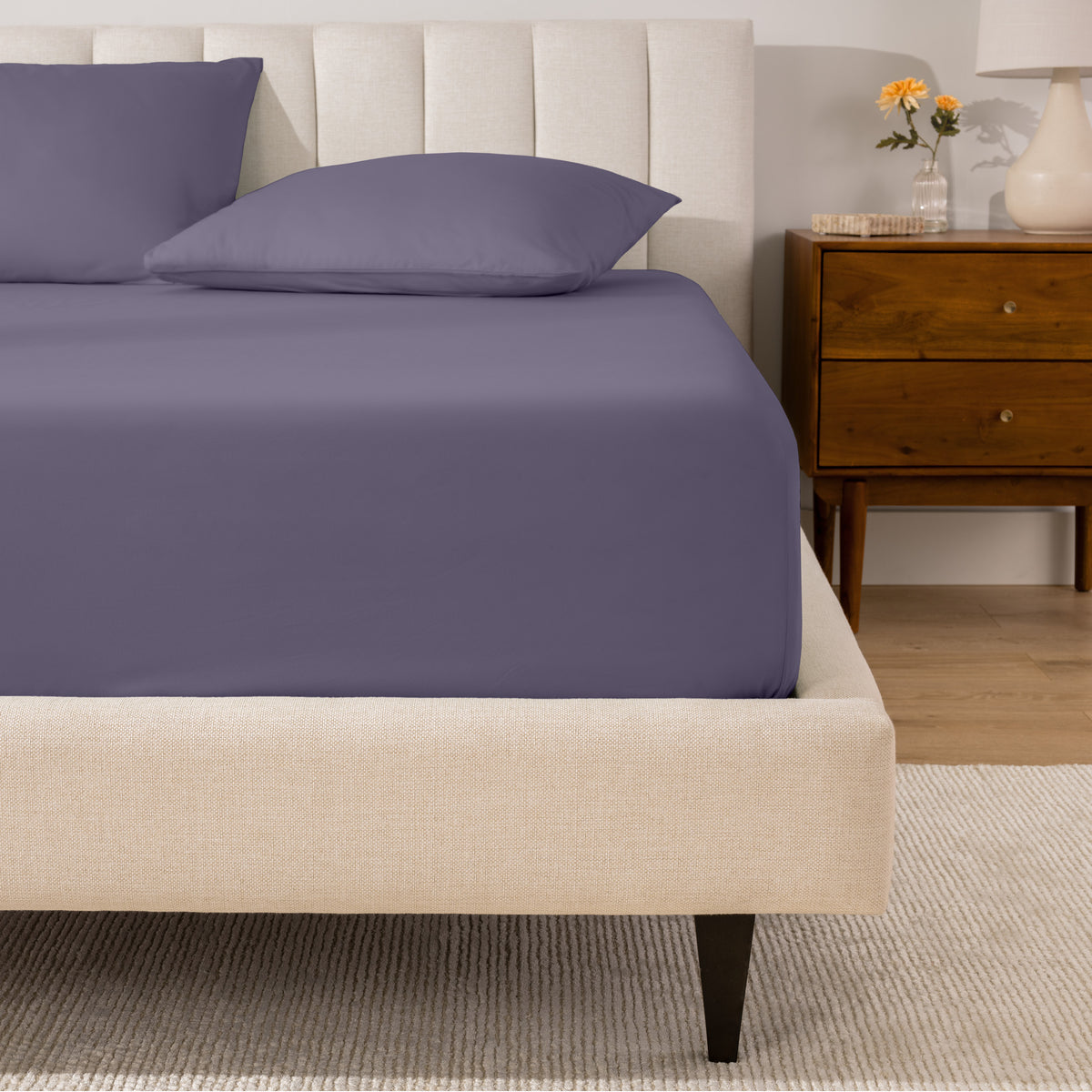 A percale fitted sheet and pillowcases on a bed in a bedroom with a wooden nightstand.