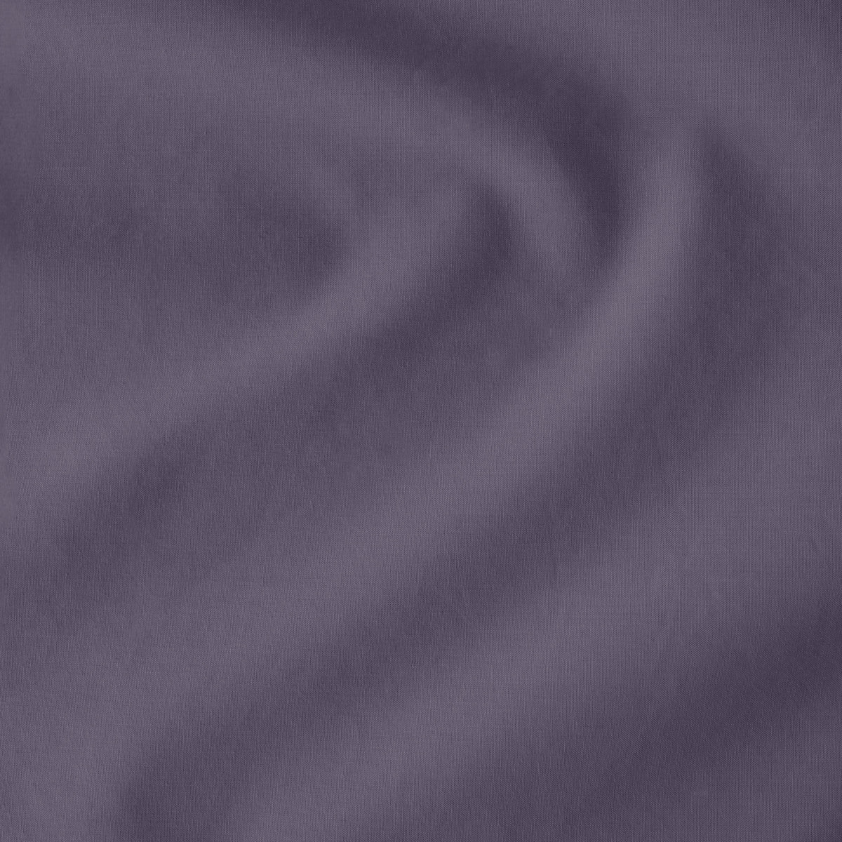 Fitted sheet on a bed with a close-up of a sewn-in tag, nightstand, lamp, and plant in a bedroom setting.