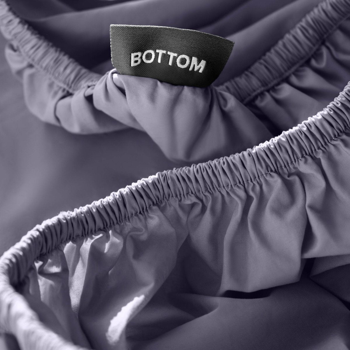 Close-up of a fitted sheet with a black fabric brand label reading BOTTOM.