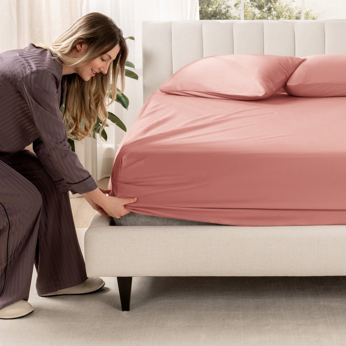 Woman adjusting a fitted sheet on a bed in a bedroom setting
