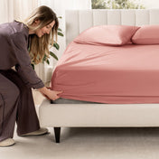 Woman adjusting a fitted sheet on a bed in a bedroom setting