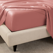 A close-up of the corner of a bed with a fitted sheet and matching flat sheet.