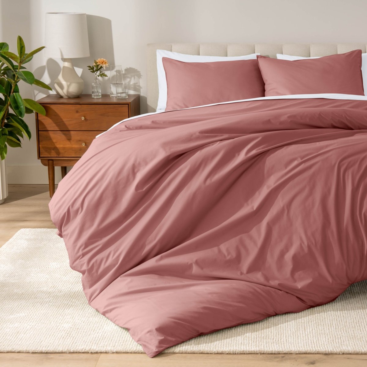 Percale bedding set on a bed in a bedroom with a wooden nightstand and lamp.