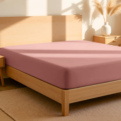 Fitted sheet on a bed in a bedroom setting with a lamp and plant.