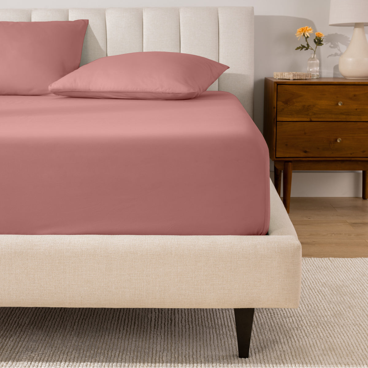 A percale fitted sheet and pillowcases on a bed in a bedroom with a wooden nightstand.