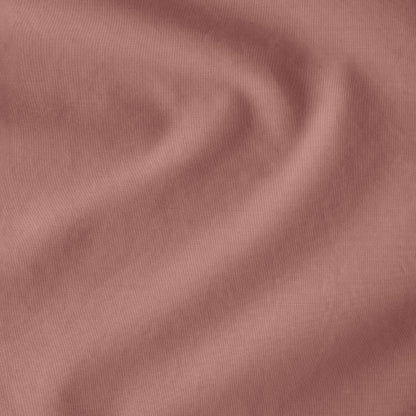 Fitted sheet on a bed with a close-up of a sewn-in tag, nightstand, lamp, and plant in a bedroom setting.