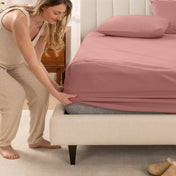 Woman in pajamas adjusting bed sheets on a bed.