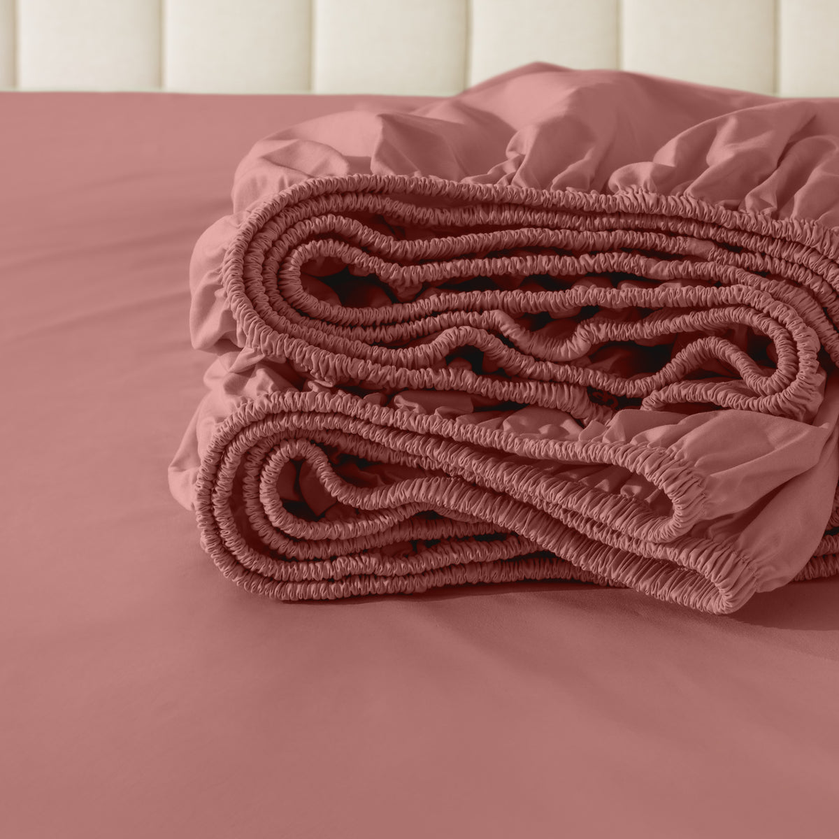 Folded fitted sheet on a bed with a neutral background