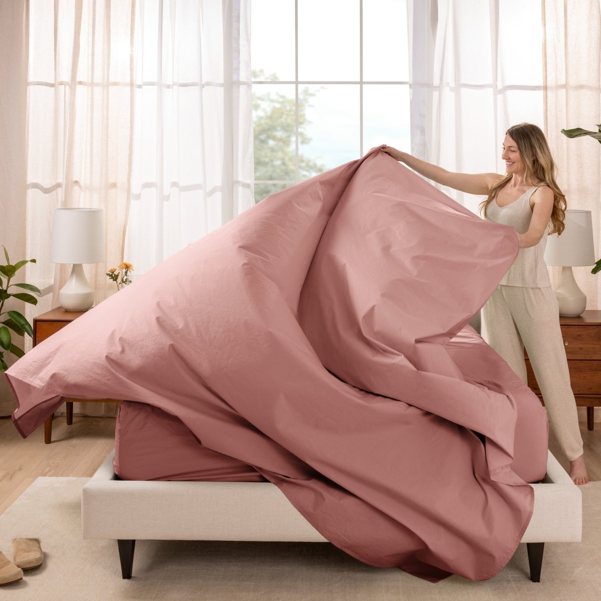 Woman putting a sheet set on a bed in a bright bedroom.