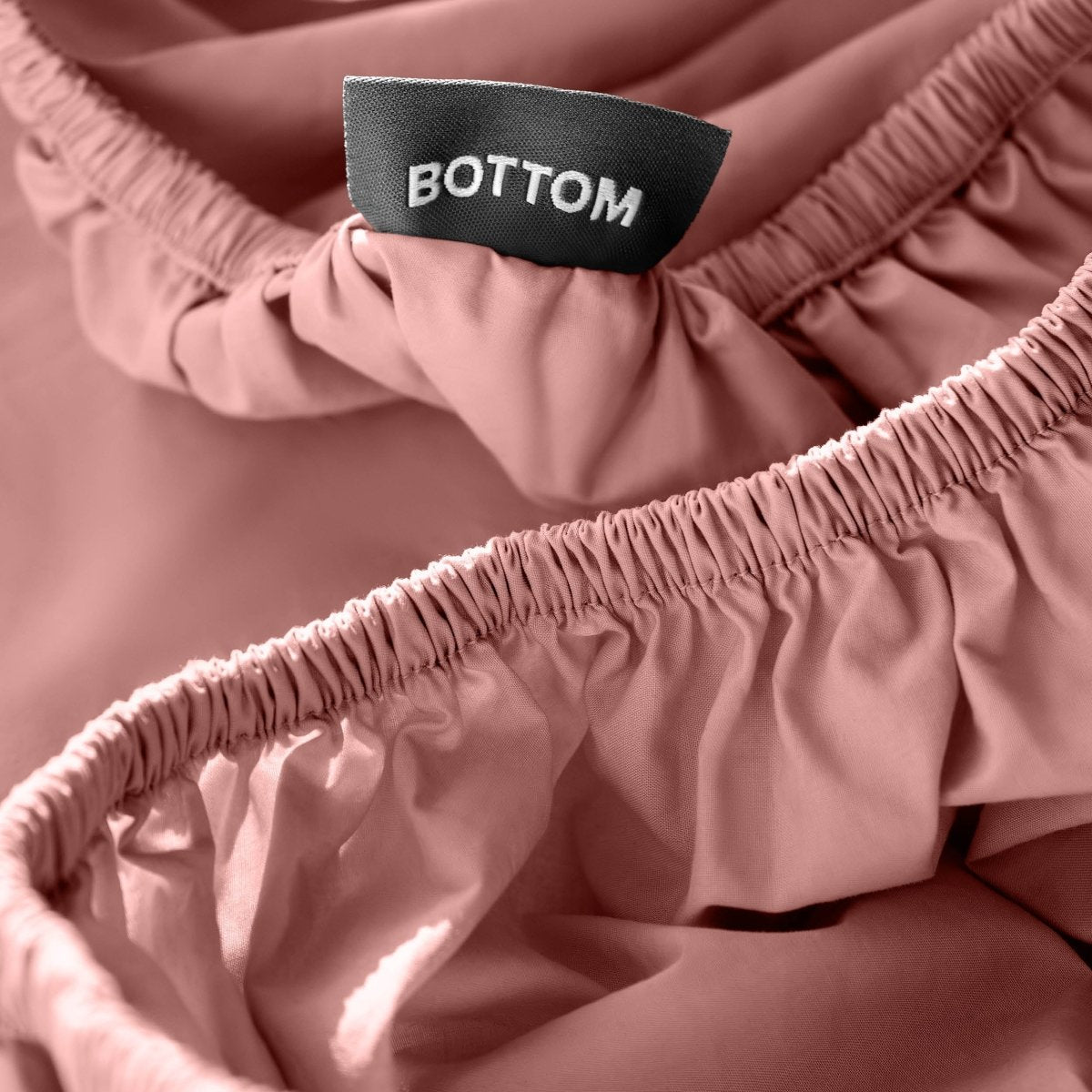 Close-up of a fitted sheet with a black fabric brand label reading BOTTOM.