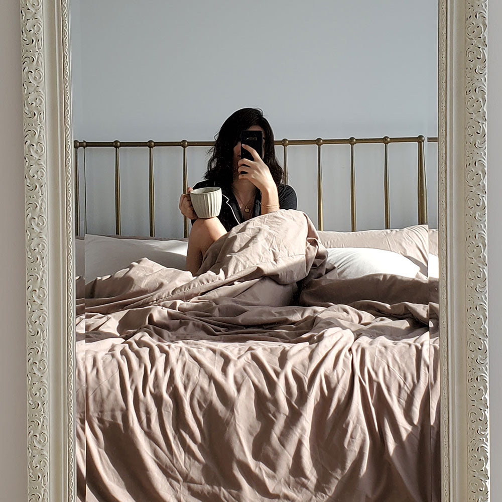 Woman drinking coffee in bed with under a taupe colored duvet cover