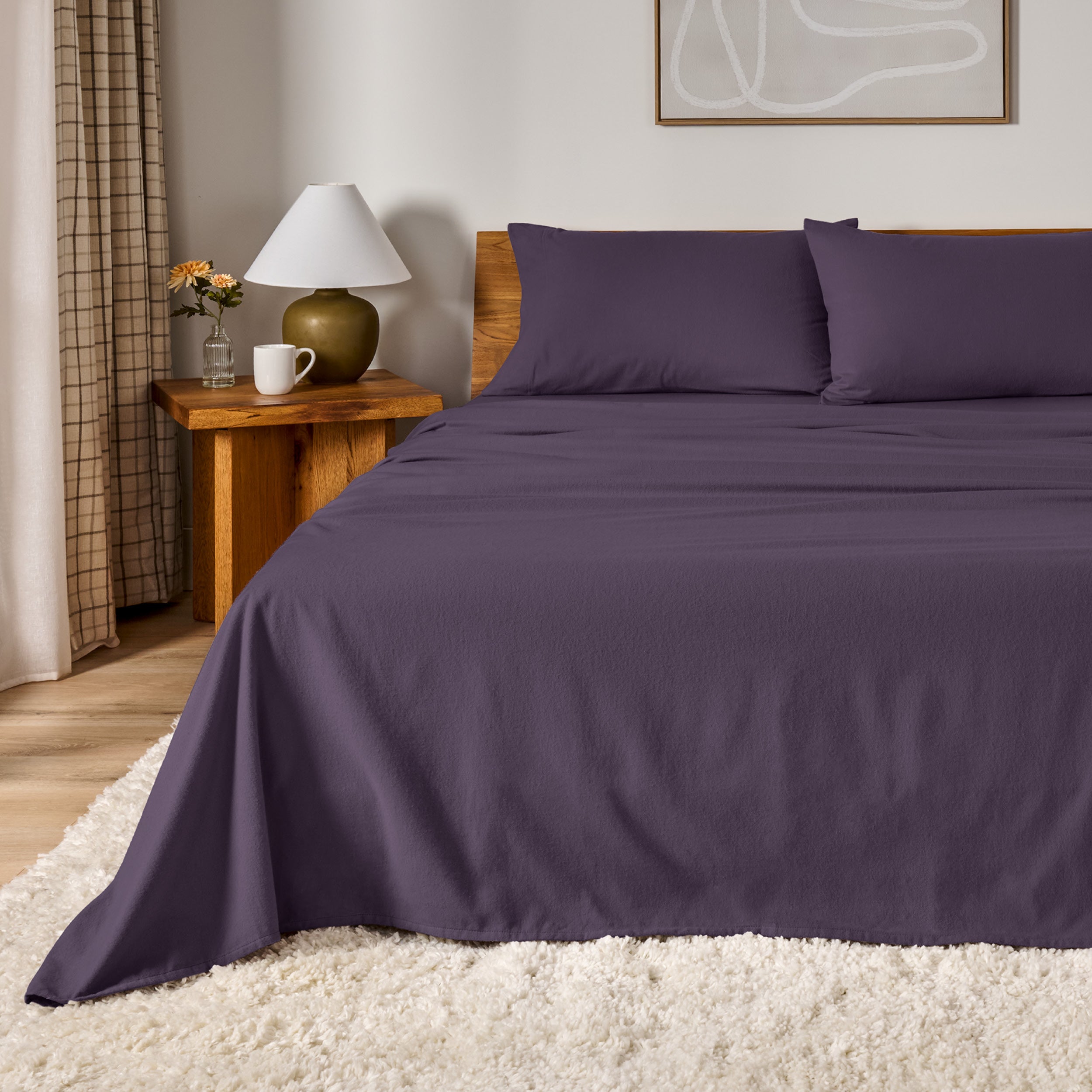A bed dressed in flannel sheet set in a bedroom with a wooden headboard, bedside table and lamp
