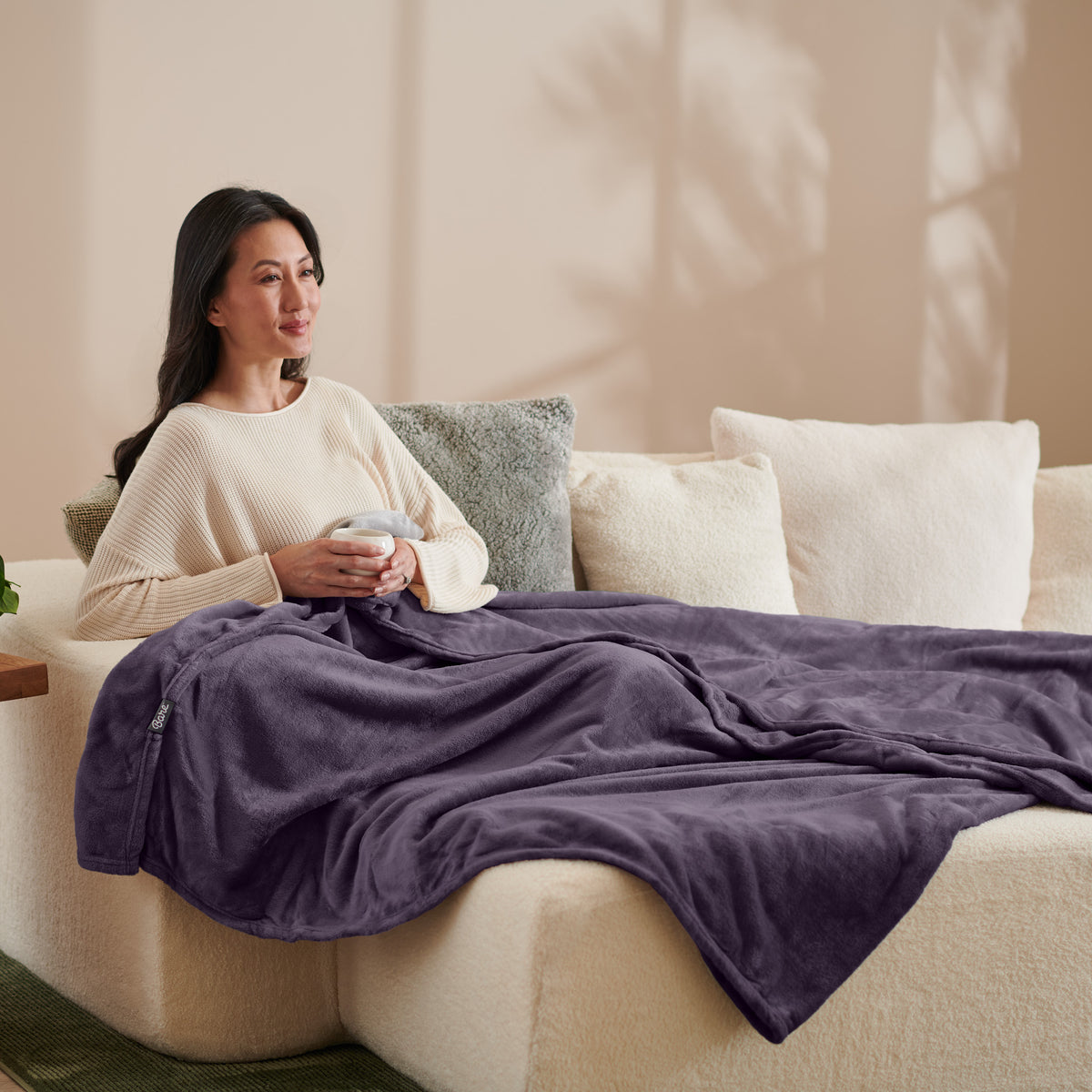 A woman sitting on a couch with a microplush blanket on her lap