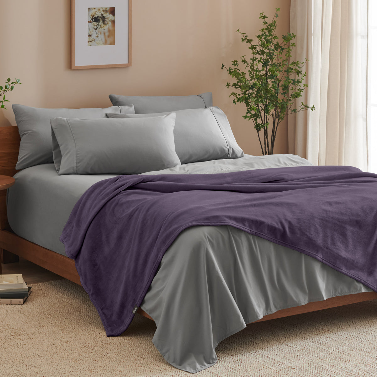 A bed made with grey sheets and a microplush blanket