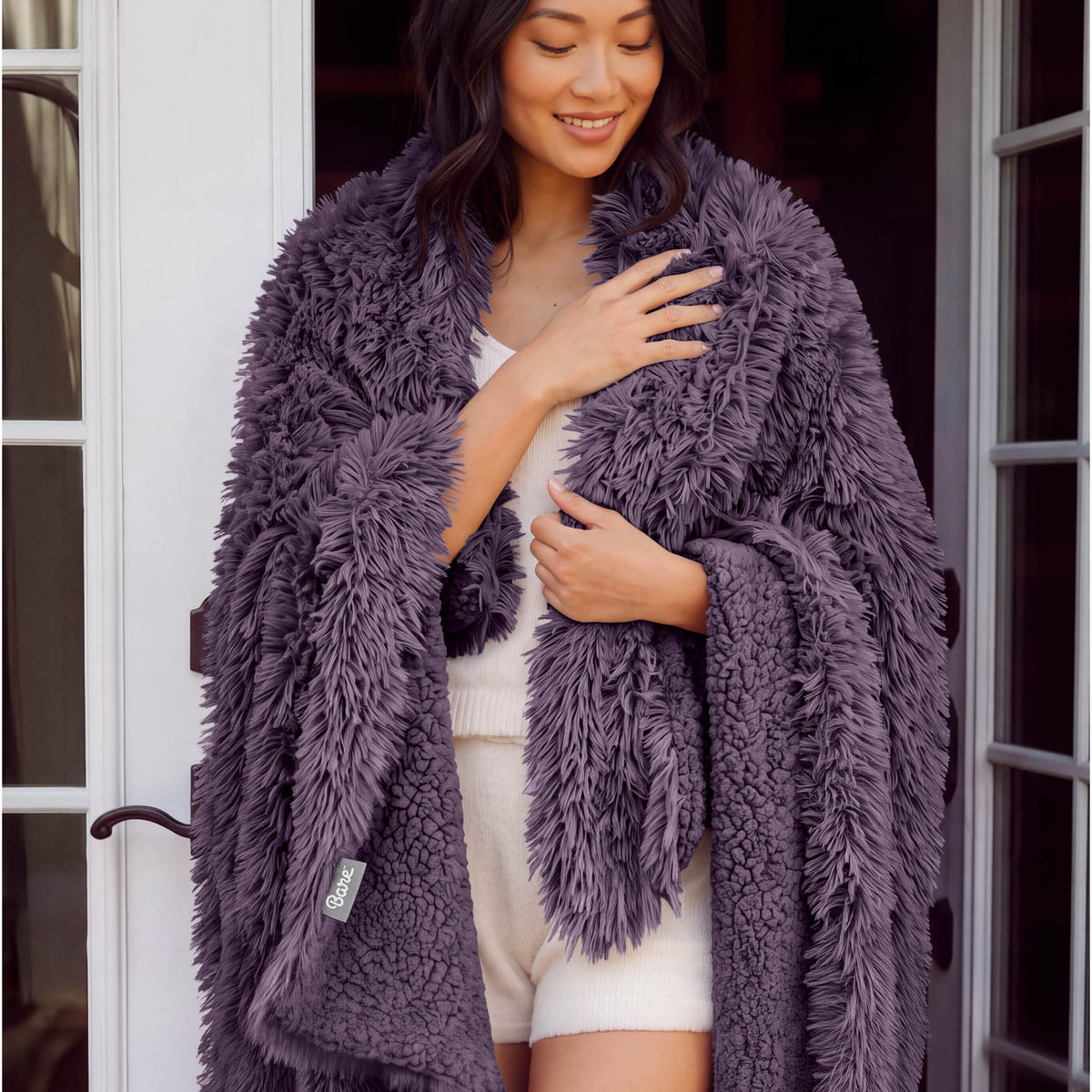 A woman standing with a shaggy blanket wrapped around her