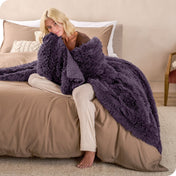 A woman sitting on the end of a bed with a shaggy blanket wrapped around her