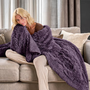 A woman sitting on a couch with a shaggy blanket wrapped around her