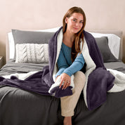 A woman sitting on a bed with a Sherpa blanket around her