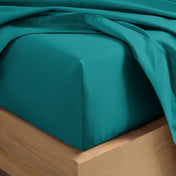 A close-up of a fitted sheet covering the corner of a bed frame, with matching top sheet draped over it.