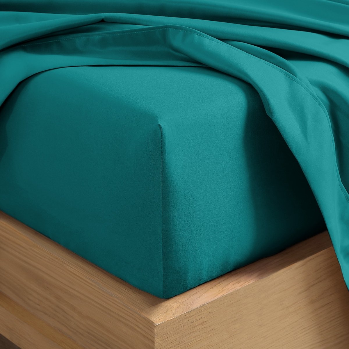 A close-up of a fitted sheet covering the corner of a bed frame, with matching top sheet draped over it.