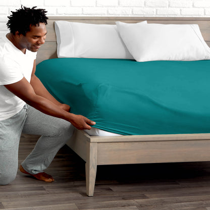 Man adjusting fitted sheet on a bed with white pillows.