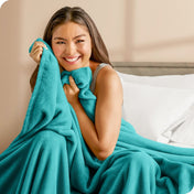 Woman sitting on a bed cuddling with a microplush blanket