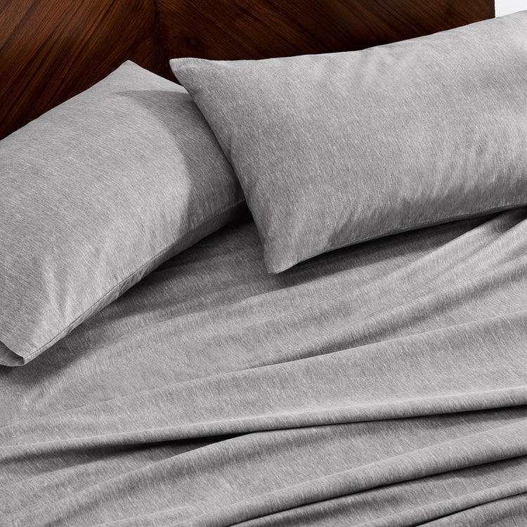 Gray bedding set with two pillows on a wooden bed frame.