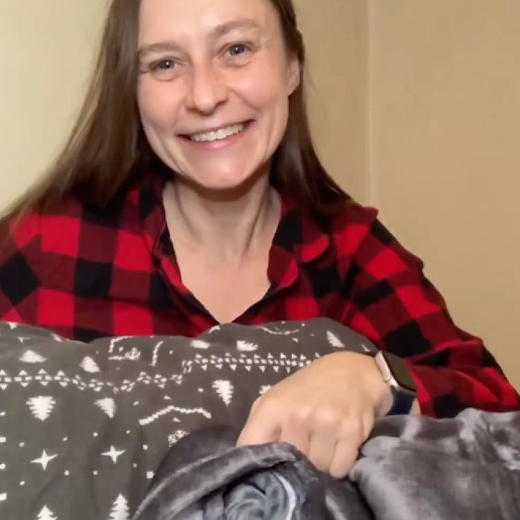 Woman wearing a red and black checkered shirt holding a blanket with a pattern.