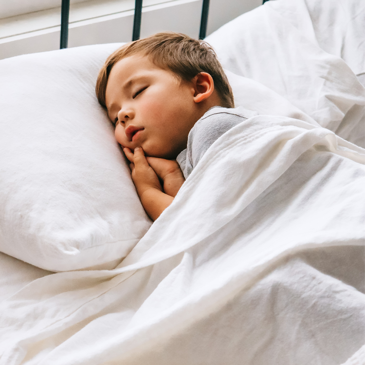 Child sleeping peacefully under white bedding in a softly lit room.