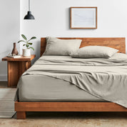 Bedroom with sheet set on a wooden bed frame, side table with plant and lamp.