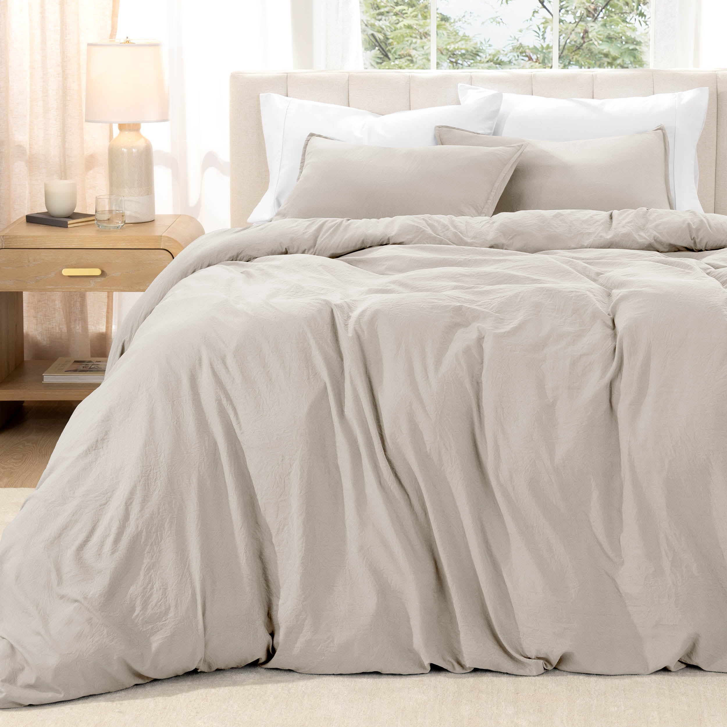 Bed with washed bedding and white pillows in a bright room