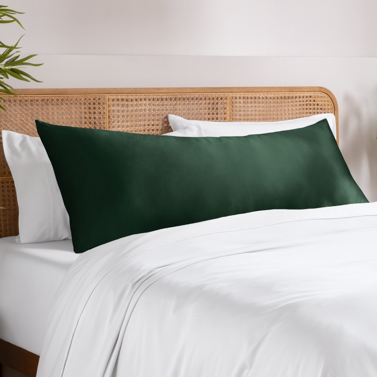 Body pillowcase on a pillow set on a bed with a wicker headboard and a plant in the corner.