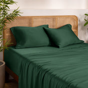 Bamboo bed sheets and pillows on a bed with a wicker headboard in a room with plants.