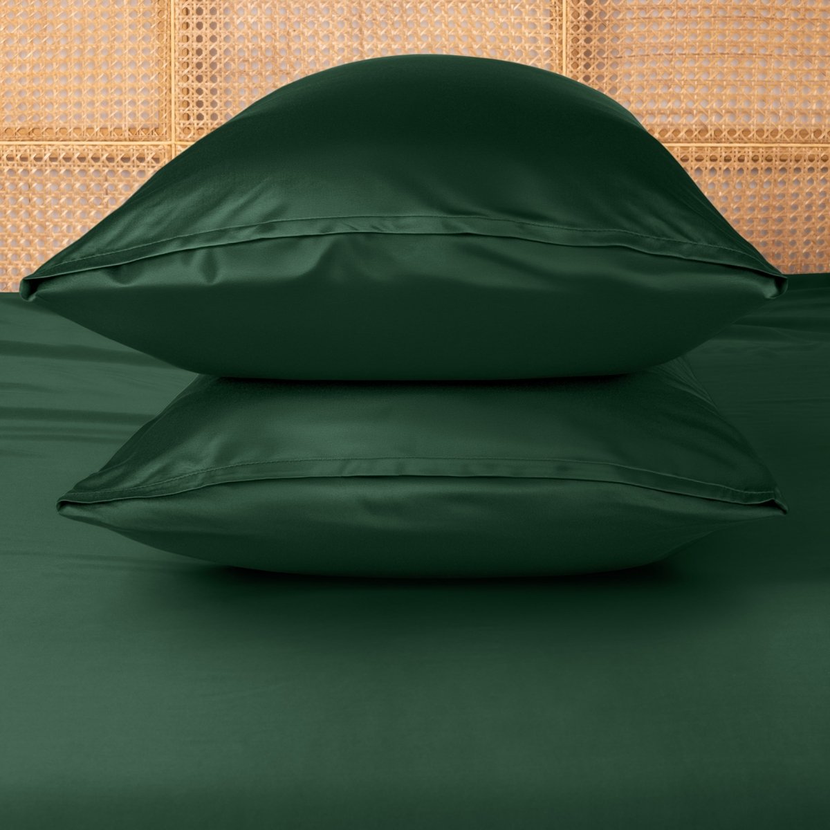 Two green pillows stacked on a bed with a woven headboard.