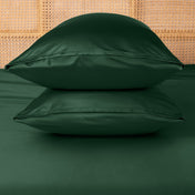 Two green pillows stacked on a bed with a woven headboard.