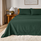 A bed dressed in flannel sheet set in a bedroom with a wooden headboard, bedside table and lamp