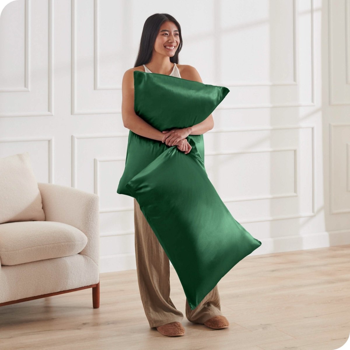 A woman standing while holding pillows with silk pillowcases on them