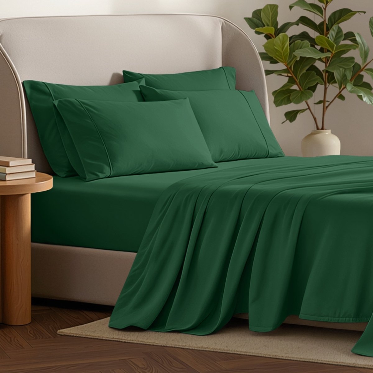 Bed sheets and pillows on a bed with a plant and side table in the background.