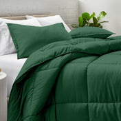 Comforter and pillow shams on a bed with a white brick wall and plant in the background