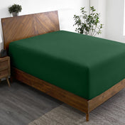 Wooden bed frame with a fitted sheet on the mattress in a room with plants and a nightstand.