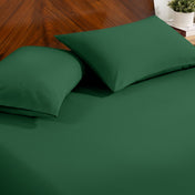 Fitted sheet and pillowcase set on a bed with a dark wood headboard and a small potted plant in the background.