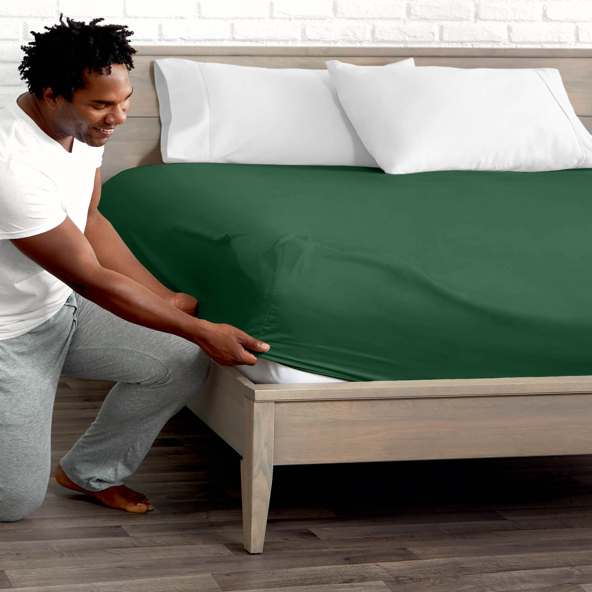 Man adjusting fitted sheet on a bed with white pillows.