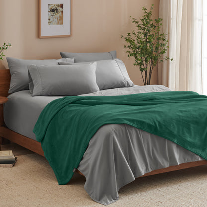 A bed made with grey sheets and a microplush blanket