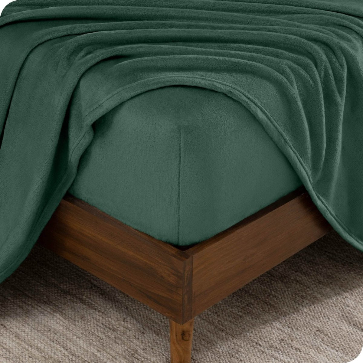 The corner of a bed frame and mattress with a fitted sheet and flat sheet on it.