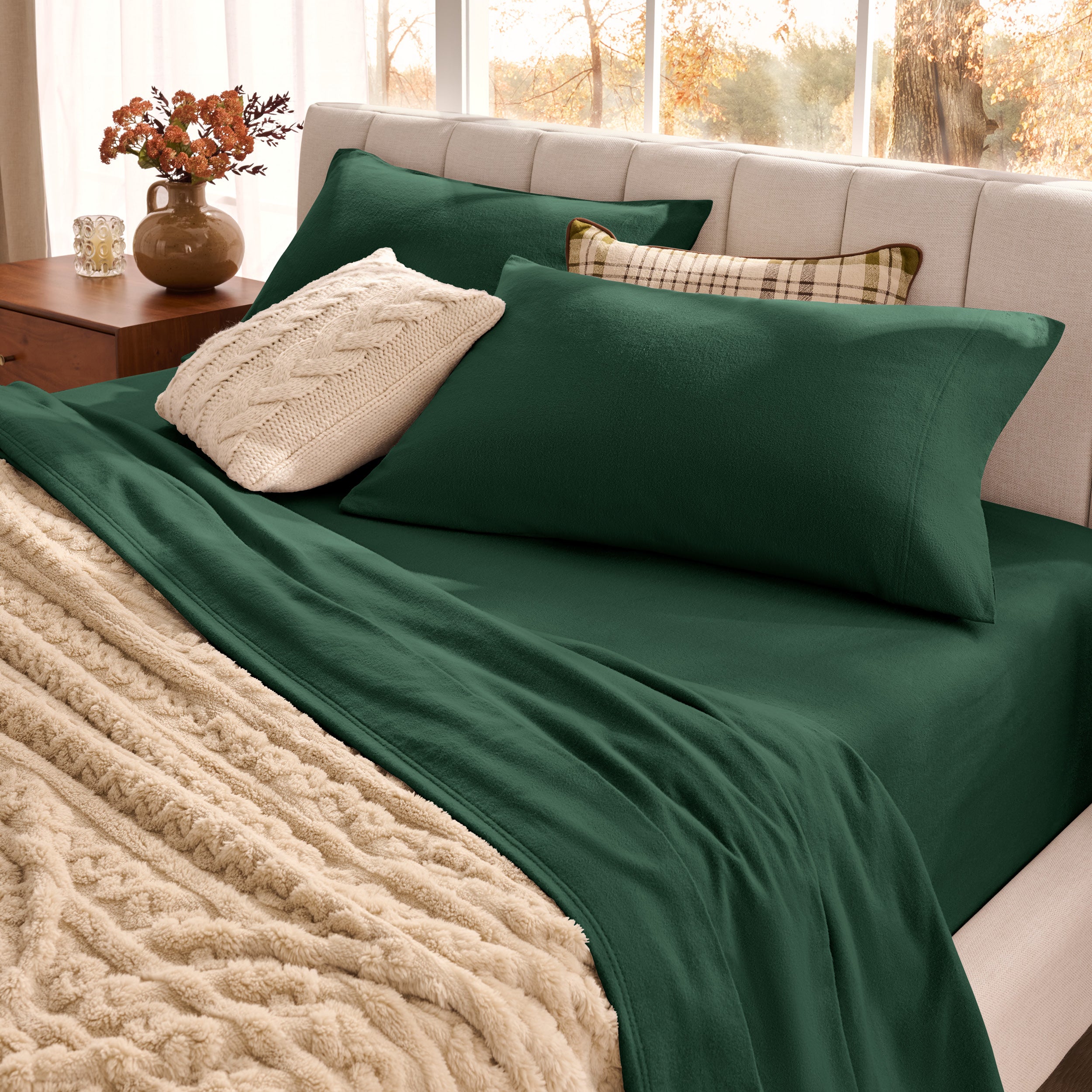 Neatly made bed with organic flannel sheets  and a beige blanket in a bright bedroom.