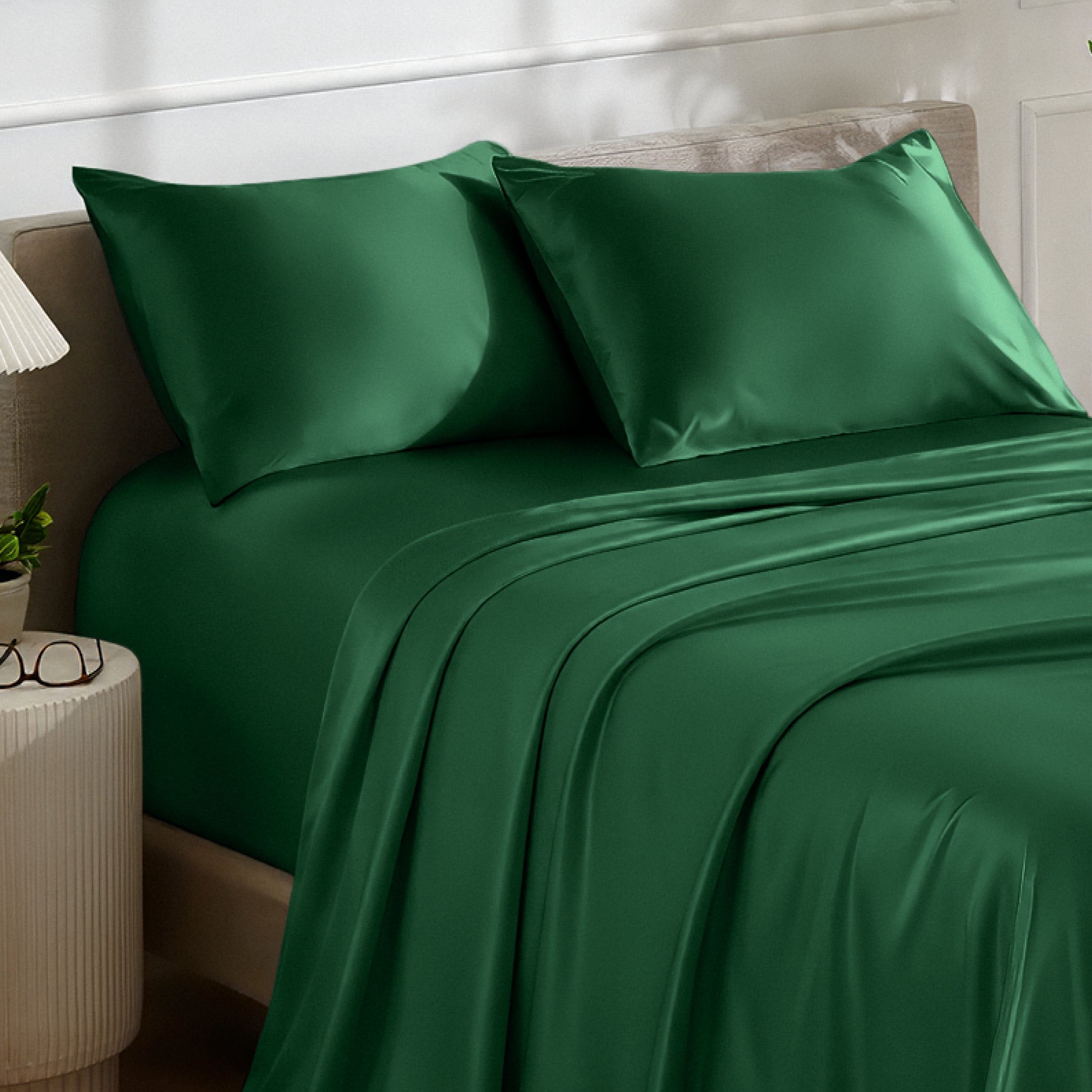 Satin bedding set on a bed with a nightstand and lamp in the background.