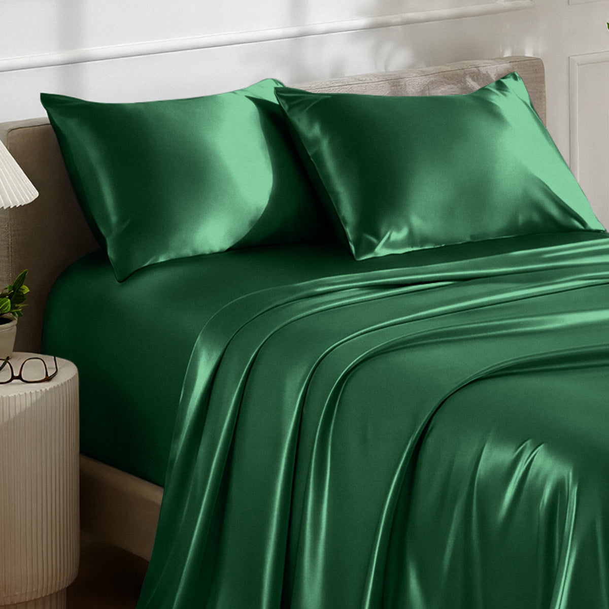 Satin bedding set on a bed with a nightstand and lamp in the background.